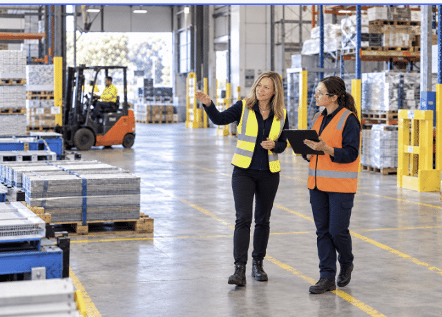 Two women in high-visibility vests discussing operations in a warehouse